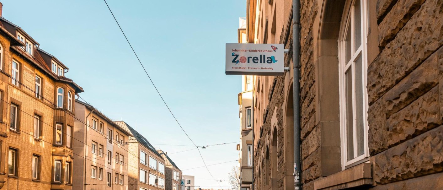 Schild des Johanniter-Kinderkaufhauses Zorella an einer Hauswand in einer sonnigen Straße mit Altbauten., © Stuttgart-Marketing GmbH, Sarah Schmid Schild des Johanniter-Kinderkaufhauses Zorella an einer Hauswand in einer sonnigen Straße mit Altbauten., © Stuttgart-Marketing GmbH, Sarah Schmid