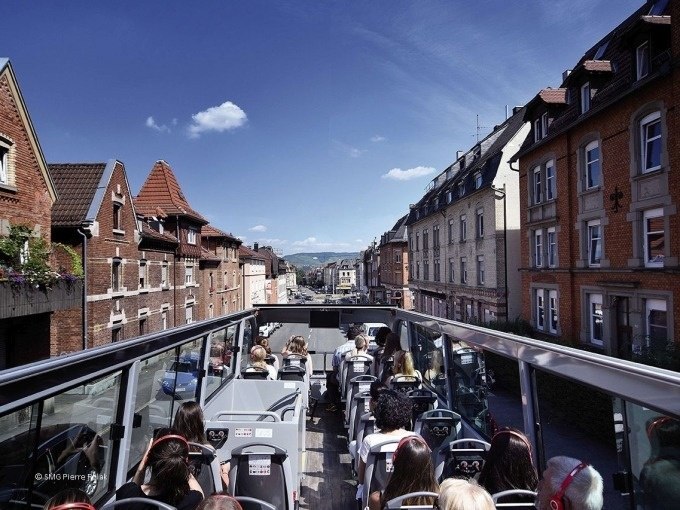 Touristen sitzen in einem offenen Doppeldeckerbus und fahren durch eine Straße in Stuttgart bei sonnigem Wetter., © SMG, Pierre Polak Touristen sitzen in einem offenen Doppeldeckerbus und fahren durch eine Straße in Stuttgart bei sonnigem Wetter., © SMG, Pierre Polak
