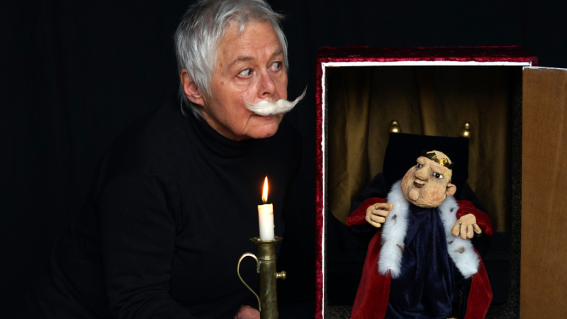 Eine Person mit falschem Schnurrbart hält eine Kerze neben einer königlichen Puppe in einem kleinen Theaterkasten., © Theater in der Badewanne