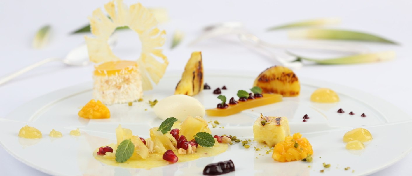 Kunstvoll angerichtetes Dessert mit Ananas, Granatapfelkernen und Minzblättern auf weißem Teller. Elegante Präsentation in der Landhaus Feckl Küche., © Landhaus Franz Feckl