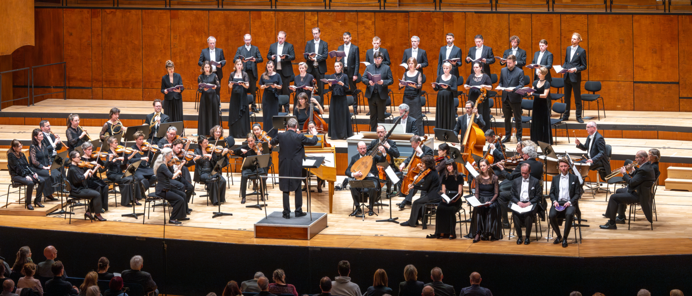 Ein Orchester und Chor in formeller Kleidung f&uuml;hren auf einer B&uuml;hne ein klassisches Konzert auf. Der Dirigent steht vor dem Orchester., &copy; Holger Schneider