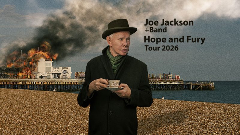 Ein Mann mit Hut und Teetasse steht vor einem brennenden Geb&auml;ude am Pier. Im Hintergrund ist Rauch zu sehen. Text: Joe Jackson & Band - Hope and Fury Tour 2026., &copy; links im Bild