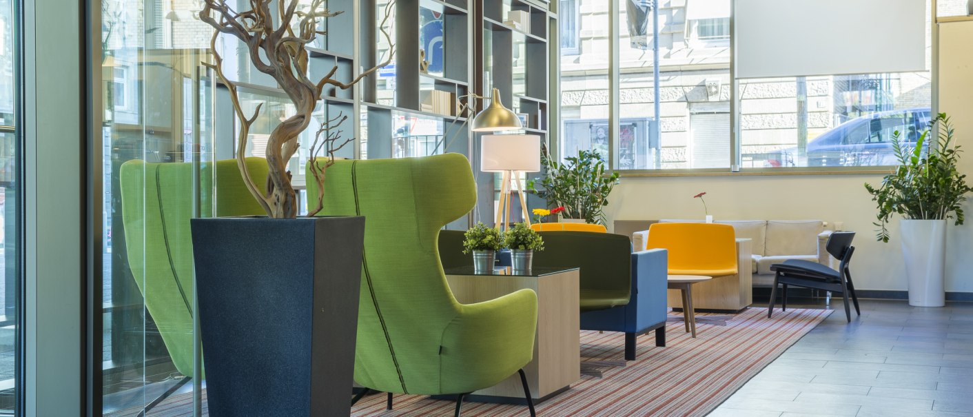 Moderne Lobby mit grünen und gelben Sesseln, Pflanzen und großen Fenstern. Ein Teppich und eine Lampe ergänzen das stilvolle Ambiente., © Park Inn by Radisson Stuttgart
