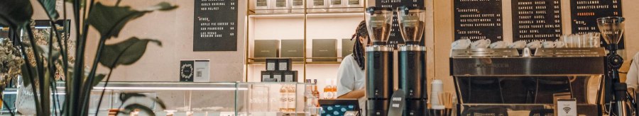 Modern caf&eacute; with counter, coffee machine and menus on the wall. Plants in the foreground, cozy atmosphere., &copy; Maison Karl, Stuttgart