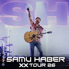 Ein Musiker steht mit Gitarre auf der B&uuml;hne, hebt die Hand. Im Hintergrund leuchtet 'SH'. Schriftzug: 'Samu Haber XX Tour 26'., &copy; links im Bild