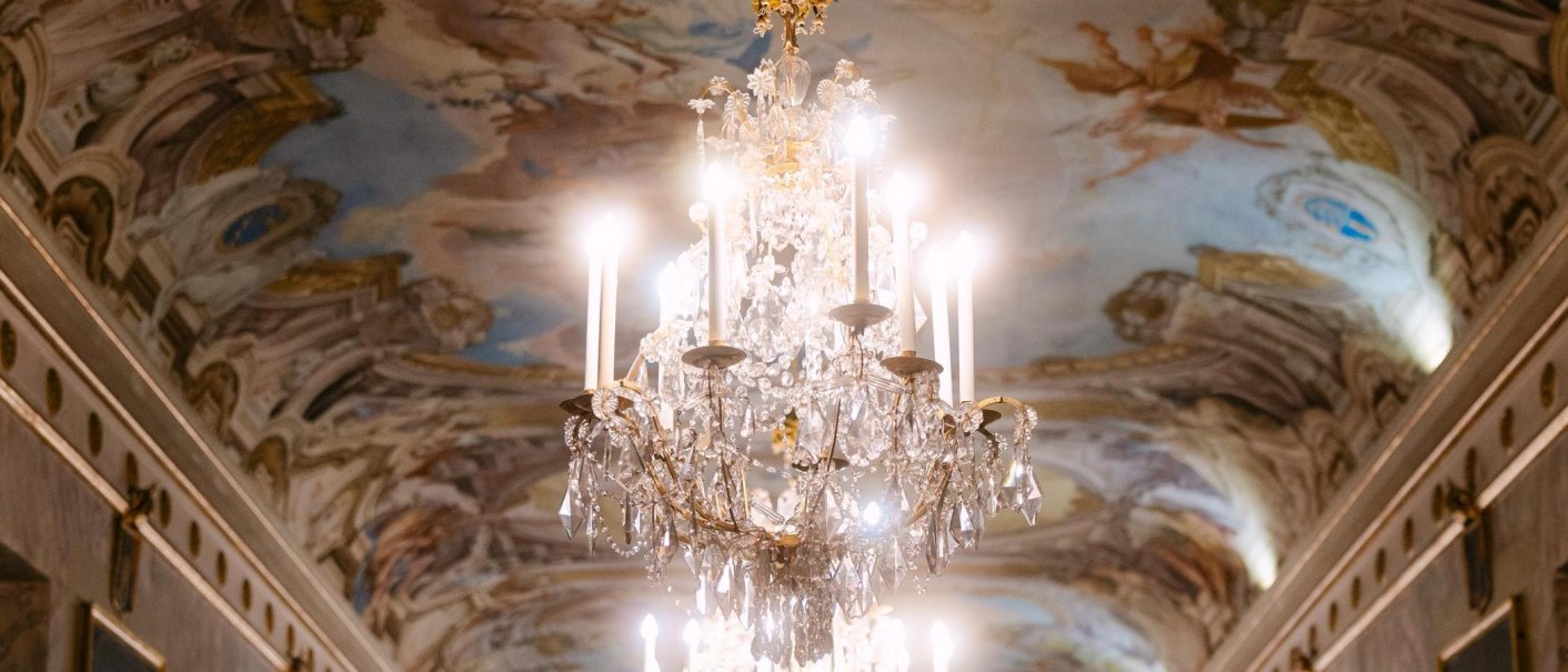 Ein funkelnder Kronleuchter h&auml;ngt unter einer kunstvoll bemalten Decke im Residenzschloss Ludwigsburg, die mit barocken Fresken verziert ist., &copy; Stuttgart-Marketing GmbH, Sarah Schmid