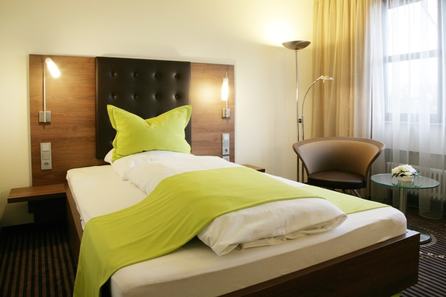 A modern single room with a bed, green bedspread, armchair and glass table in front of a window with curtains., © Hotel Fuchsen A modern single room with a bed, green bedspread, armchair and glass table in front of a window with curtains., © Hotel Fuchsen