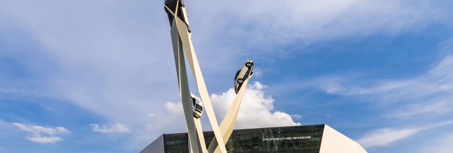 The Porsche Museum with its modern architecture and a sculpture of three cars on high pillars against a blue sky., © Stuttgart-Marketing GmbH, Werner Dieterich
