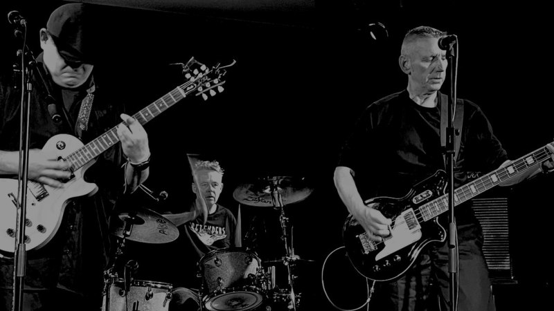 Eine Band spielt auf der B&uuml;hne. Zwei Gitarristen und ein Schlagzeuger sind in Aktion. Das Bild ist in Schwarz-Wei&szlig; gehalten., &copy; Herz Rhythmus Maschine