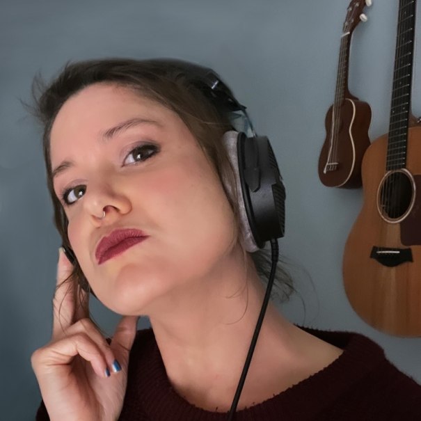 Eine Frau tr&auml;gt Kopfh&ouml;rer und posiert vor einer Wand mit Gitarren. Sie hat einen nachdenklichen Ausdruck und ber&uuml;hrt den Kopfh&ouml;rer mit der Hand., &copy; Rosenau Kultur e.V.