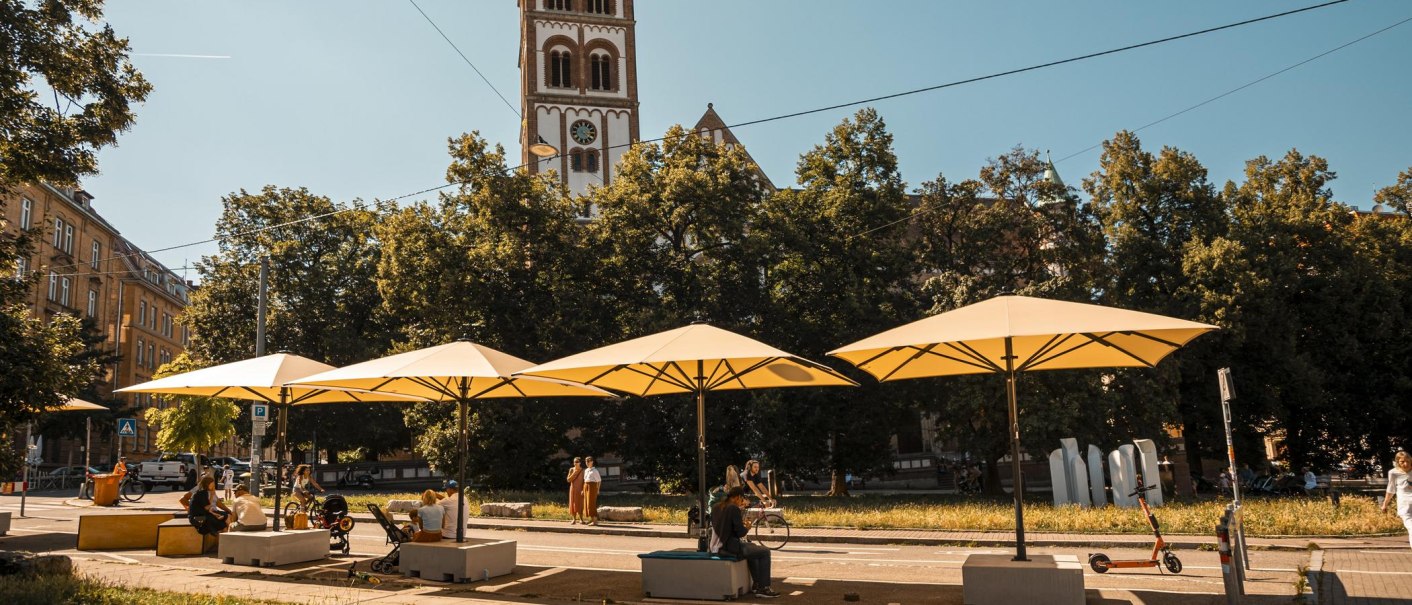 Bismarckplatz mit gelben Sonnenschirmen und Sitzgelegenheiten. Im Hintergrund ein Kirchturm und Bäume unter klarem Himmel., © SMG, Sarah Schmid Bismarckplatz mit gelben Sonnenschirmen und Sitzgelegenheiten. Im Hintergrund ein Kirchturm und Bäume unter klarem Himmel., © SMG, Sarah Schmid
