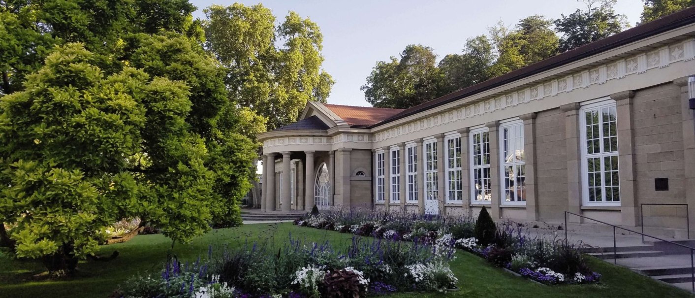 Der Kursaal Bad Cannstatt mit klassischer Architektur, großen Fenstern und einem gepflegten Garten im Vordergrund, umgeben von Bäumen., © Stuttgart-Marketing GmbH