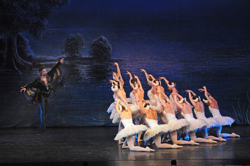 Ballettszene aus "Schwanensee" mit Tänzern in weißen Tutus und einem Tänzer in schwarzem Kostüm vor einer See-Kulisse., © Go 2 - Convent GmbH