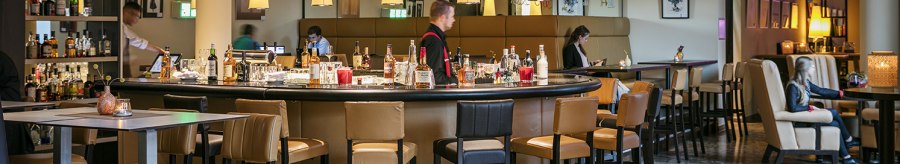Modern bar with round counter, hanging lamps and seating areas in the Arcotel Camino. People sit and enjoy the atmosphere., &copy; &copy; Harald Eisenberger