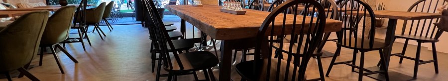 Ein stilvoll eingerichtetes Restaurant mit Holztischen, schwarzen St&uuml;hlen und einer Decke voller Lichterketten., &copy; heavenskitchen
