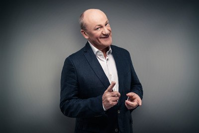 Ein Mann in einem dunklen Anzug l&auml;chelt und zeigt mit dem Finger in die Kamera vor einem grauen Hintergrund., &copy; Renitenztheater Stuttgart e.V.