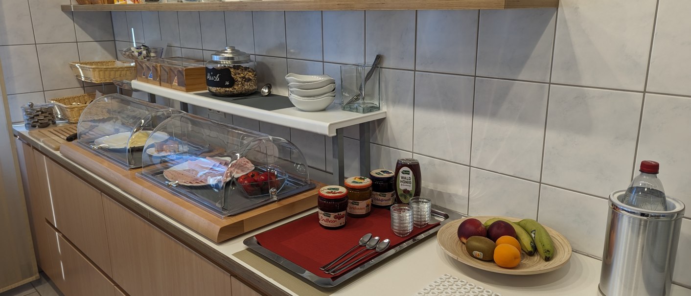 Ein Frühstücksbuffet mit Aufschnitt, Marmeladen, Müsli, Obst und Getränken auf einer Theke in einer Küche., © Gästehaus Ziegler Ein Frühstücksbuffet mit Aufschnitt, Marmeladen, Müsli, Obst und Getränken auf einer Theke in einer Küche., © Gästehaus Ziegler