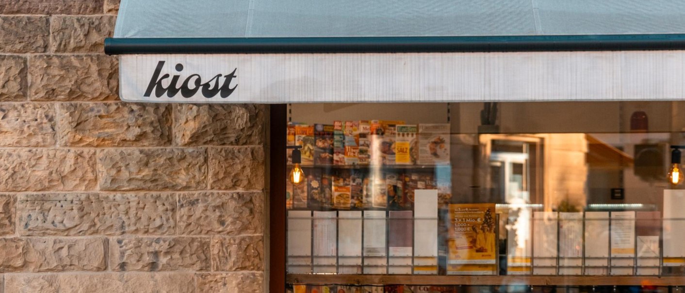 Ein Kiosk mit der Aufschrift 'kiost' zeigt Zeitschriften im Schaufenster. Die Steinwand und das Licht schaffen eine gemütliche Atmosphäre., © Stuttgart-Marketing GmbH, Sarah Schmid Ein Kiosk mit der Aufschrift 'kiost' zeigt Zeitschriften im Schaufenster. Die Steinwand und das Licht schaffen eine gemütliche Atmosphäre., © Stuttgart-Marketing GmbH, Sarah Schmid
