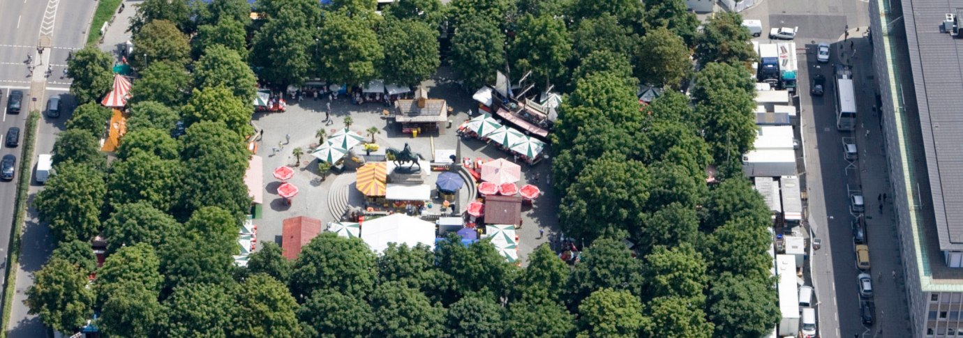 Luftaufnahme des Karlsplatzes in Stuttgart. Marktst&auml;nde und bunte Sonnenschirme sind von B&auml;umen umgeben. Eine Reiterstatue steht zentral., &copy; Stuttgart-Marketing GmbH