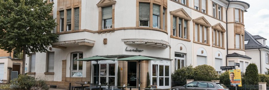 Ein Café namens Lamber an einer Straßenecke mit Außensitzbereich und einem geparkten Auto davor., © Stuttgart Marketing GmbH, Sarah Schmid Ein Café namens Lamber an einer Straßenecke mit Außensitzbereich und einem geparkten Auto davor., © Stuttgart Marketing GmbH, Sarah Schmid