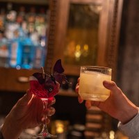 Two men clinking cocktails in a bar, one in a checked jacket, the other in a light-colored shirt. Bottles can be seen in the background., &copy; &copy; Stuttgart-Marketing GmbH, Martina Denker