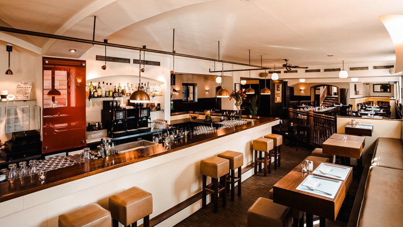 A stylish restaurant with a bar, wooden furniture and modern lighting. The bar is well stocked and there is seating with covered tables., © Amadeus