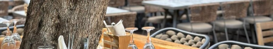 An outdoor restaurant table with a tree in the middle, surrounded by chairs. The table is set with glasses and cutlery., &copy; &copy;Meze Meze