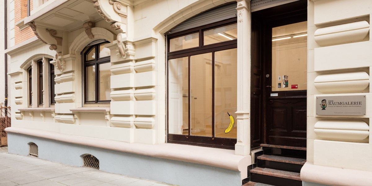 Eingang einer Galerie mit dem Schild 'Die Raumgalerie'. Eine Banane ist an der Glastür angebracht. Das Gebäude hat eine verzierte Fassade., © Dirk Wilhelmy Fotografie Eingang einer Galerie mit dem Schild 'Die Raumgalerie'. Eine Banane ist an der Glastür angebracht. Das Gebäude hat eine verzierte Fassade., © Dirk Wilhelmy Fotografie
