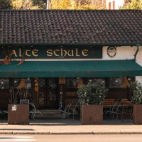 A cozy building with the sign 'Alte Schule' (old school), surrounded by plants. A man sits on a bench while another looks at his cell phone., &copy; SMG Stuttgart Marketing GmbH - Sarah Schmid