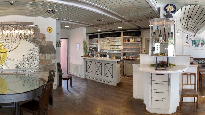 Rustikales Restaurant mit Holzmöbeln, Bar und dekorativer Wand mit "Sonnen-Besen"-Motiv. Gemütliche Atmosphäre mit Kronleuchter und Weinregal., © Weingut Zaiß