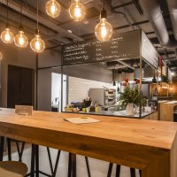 Modernes Caf&eacute; mit Holztischen, Getr&auml;nkek&uuml;hlschrank und h&auml;ngenden Gl&uuml;hbirnen. An der Wand steht "Martha's". Gem&uuml;tliche Atmosph&auml;re mit Barbereich., &copy; Martha's, Stuttgart