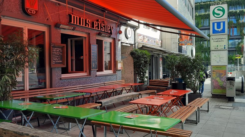 Außenbereich eines Cafés namens Mos Eisley mit bunten Tischen und Bänken. Daneben ein S- und U-Bahn-Schild am Rotebühlplatz Stadtmitte., © SMG