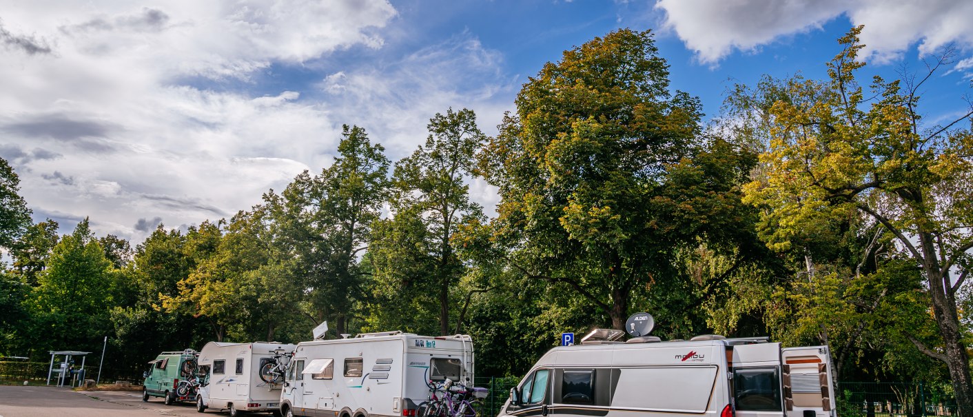 Wohnmobile parken auf einem Stellplatz in Ludwigsburg, umgeben von grünen Bäumen und einem bewölkten blauen Himmel., © Stuttgart-Marketing GmbH, Thomas Niedermüller Wohnmobile parken auf einem Stellplatz in Ludwigsburg, umgeben von grünen Bäumen und einem bewölkten blauen Himmel., © Stuttgart-Marketing GmbH, Thomas Niedermüller