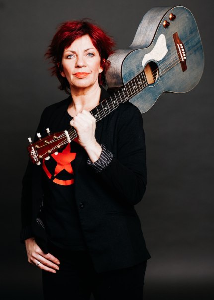 Frau mit rotem Haar h&auml;lt eine Gitarre auf der Schulter. Sie tr&auml;gt ein schwarzes Outfit und steht vor einem dunklen Hintergrund., &copy; Rosenau Kultur e.V.