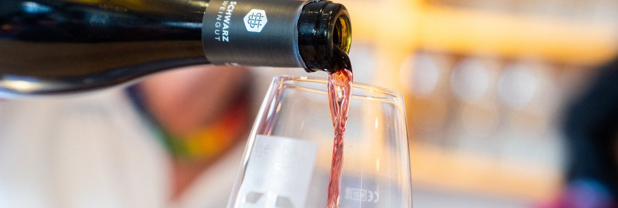 Eine Weinflasche gießt Rotwein in ein Glas. Der Hintergrund ist unscharf, der Fokus liegt auf dem fließenden Wein., © Stuttgart-Marketing GmbH, Thomas Niedermüller