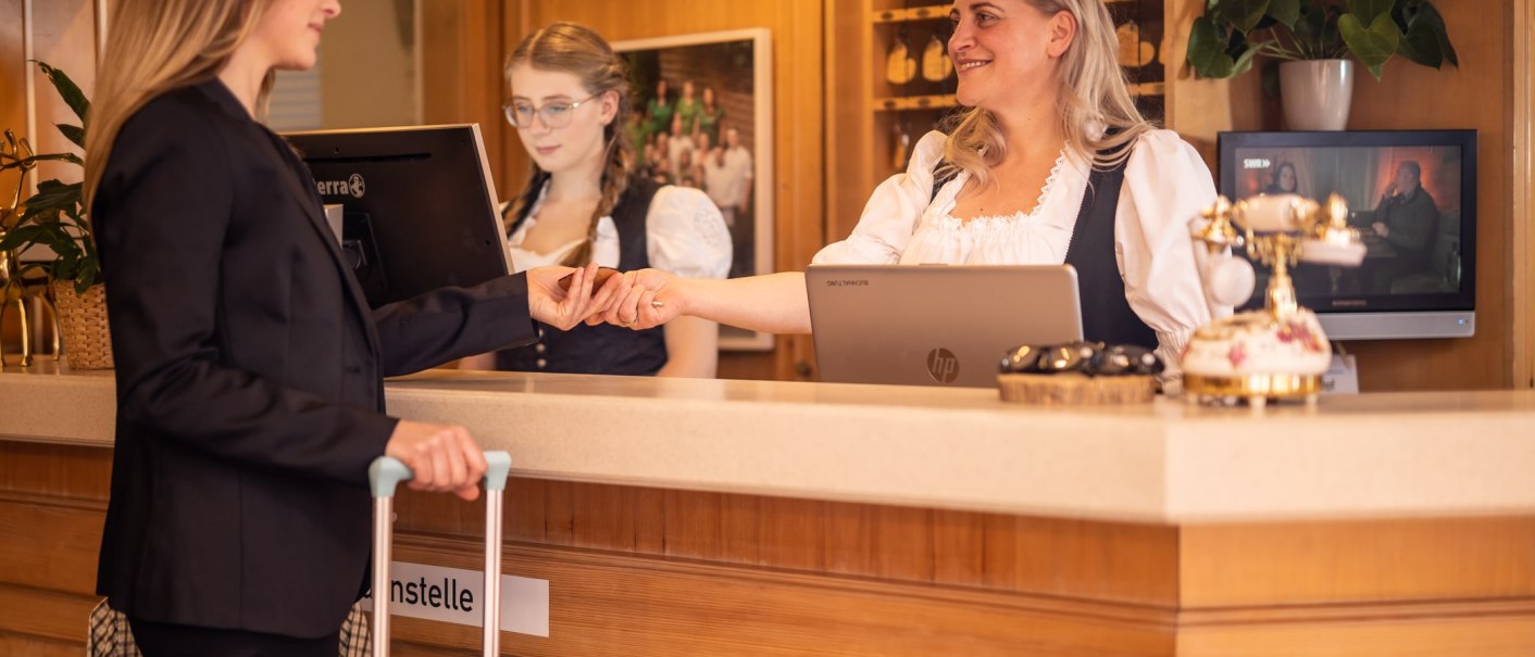 A woman at a hotel reception hands a key to another woman. Both are smiling. Another employee can be seen in the background., &copy; TOMAS
