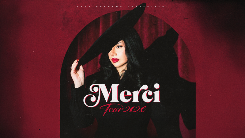 Eine Frau in schwarzem Outfit und Hut posiert vor einem roten Hintergrund. Der Text 'Merci Tour 2026' ist prominent zu sehen., &copy; links im Bild