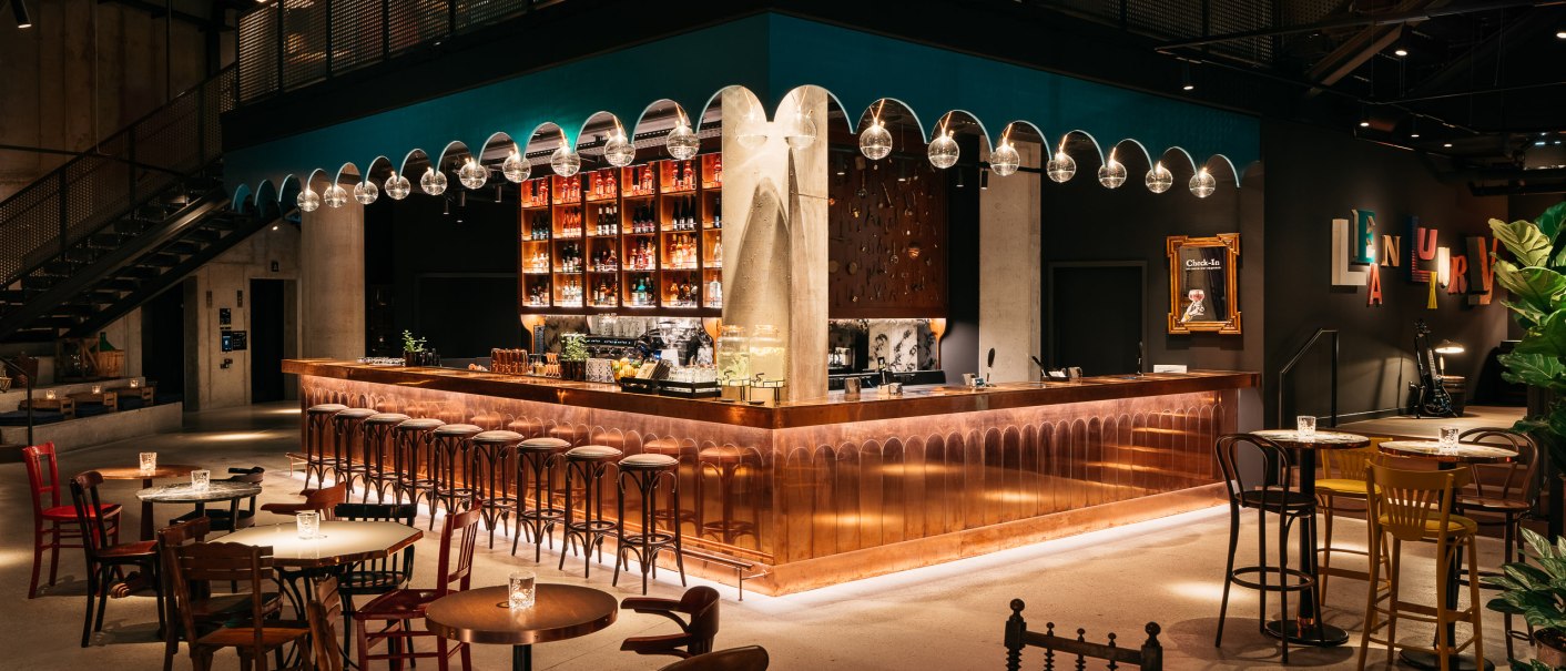 Stylish bar with copper counter, hanging glass globe lights and cozy seating areas. Modern furnishings with warm lighting and decorative elements., © © Ruby Hotels Stylish bar with copper counter, hanging glass globe lights and cozy seating areas. Modern furnishings with warm lighting and decorative elements., © © Ruby Hotels