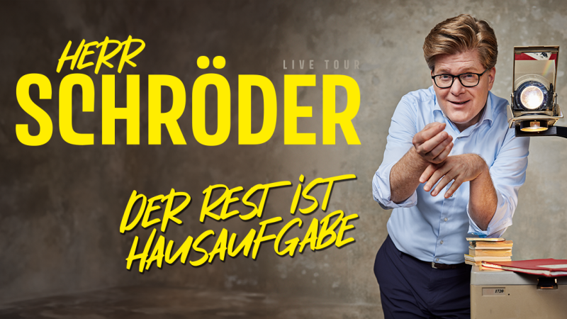 Ein Mann in einem blauen Hemd steht neben einem Overheadprojektor und l&auml;chelt. Der Text 'Herr Schr&ouml;der - Der Rest ist Hausaufgabe' ist prominent dargestellt., &copy; links im Bild