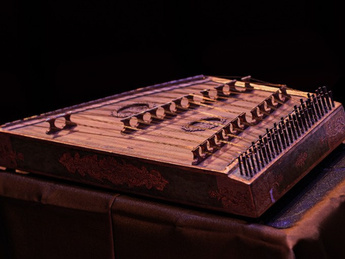 Ein traditionelles Saiteninstrument mit mehreren Saiten und Verzierungen, auf einem Tisch platziert, vor einem dunklen Hintergrund., &copy; Landesmuseum W&uuml;rttemberg