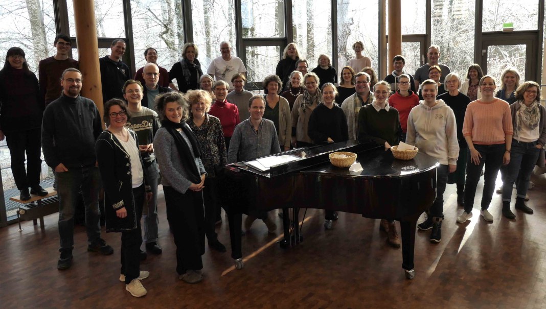 Eine Gruppe von Menschen steht um einen Flügel in einem Raum mit großen Fenstern. Sie lächeln und posieren für ein Foto., © Uni Hohenheim / Uni-Chor