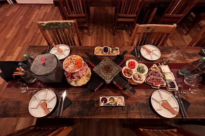 A table with raclette grill, plates, cutlery and various ingredients for a raclette evening, including vegetables, meat and sauces., &copy; Cool-Tours StattReisen