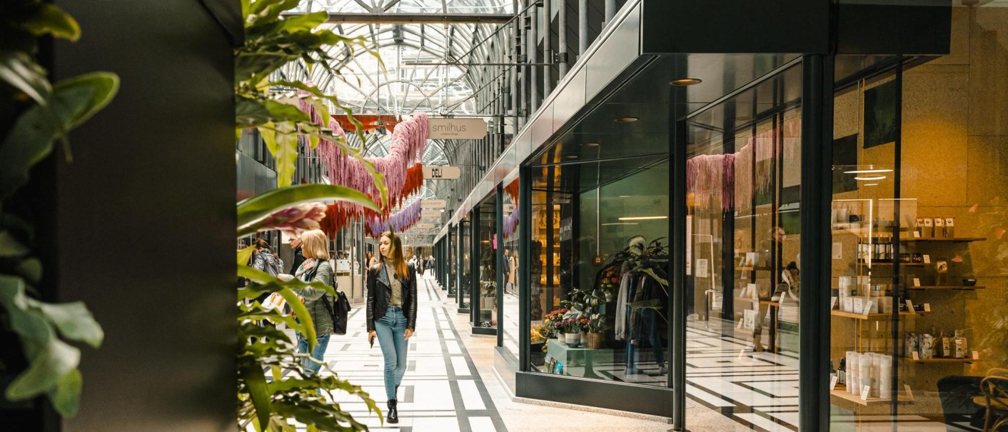 Die Calwer Passage zeigt eine moderne Einkaufspassage mit Glasdach, Geschäften und Passanten. Pflanzen und Dekorationen schmücken den Weg., © Stuttgart-Marketing GmbH, Sarah Schmid