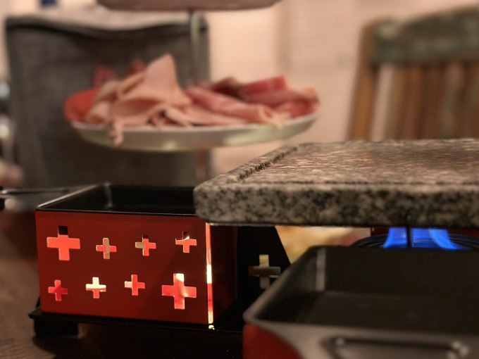 Raclette grill with red housing and stone plate, in the background cold cuts on a plate., © Cool-Tours StattReisen Raclette grill with red housing and stone plate, in the background cold cuts on a plate., © Cool-Tours StattReisen