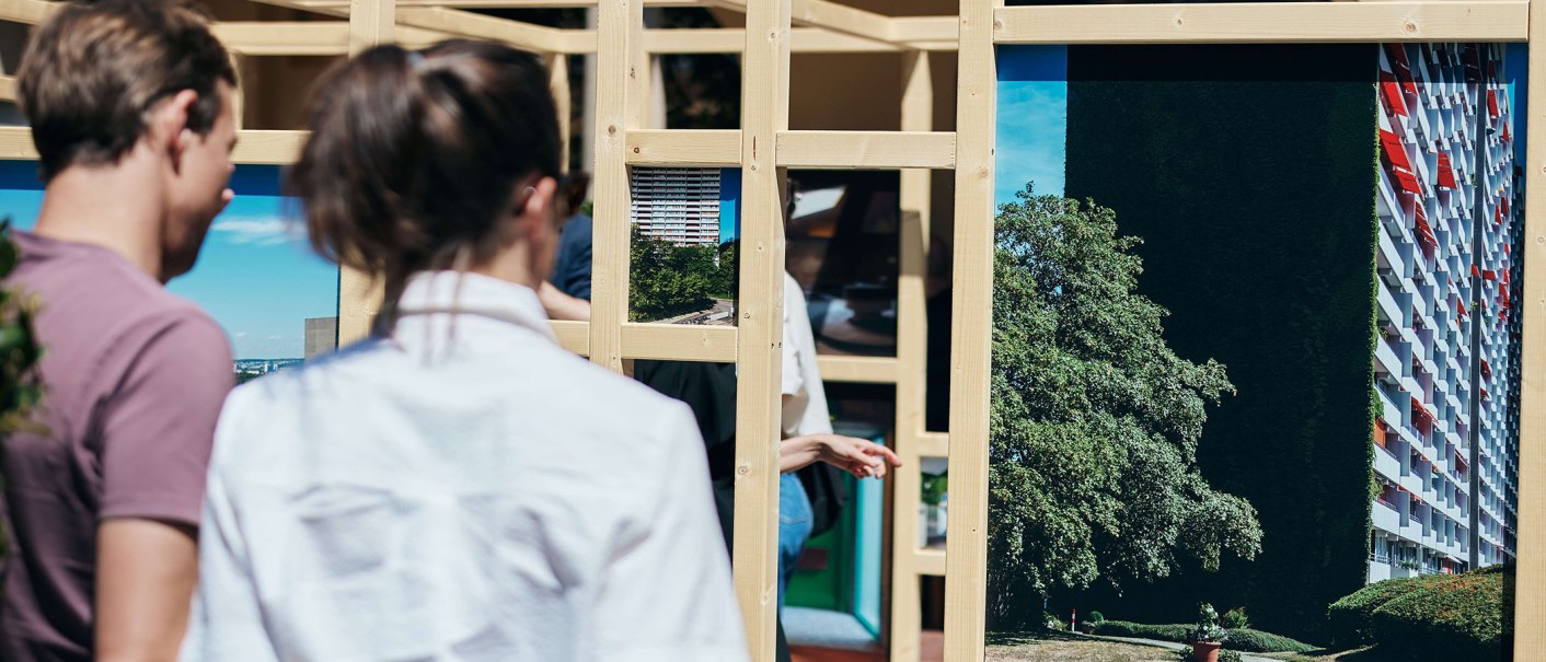 Two people look at an installation of wooden frames with photos of buildings and landscapes., © © Städtisches Lapidarium, Foto Julia Ochs