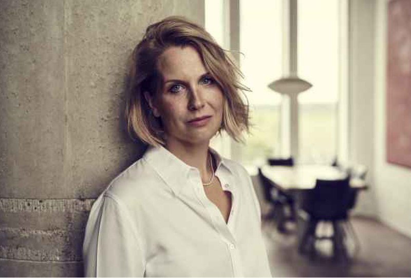 Frau in wei&szlig;em Hemd lehnt an einer Betonwand, im Hintergrund ein Tisch mit St&uuml;hlen und gro&szlig;e Fenster., &copy; Internationale Hugo-Wolf-Akademie