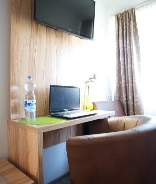 Hotel room with desk, laptop, flat-screen TV on the wall, brown armchair and window with curtains., © Hotel Reinhardtshof Garni Hotel room with desk, laptop, flat-screen TV on the wall, brown armchair and window with curtains., © Hotel Reinhardtshof Garni