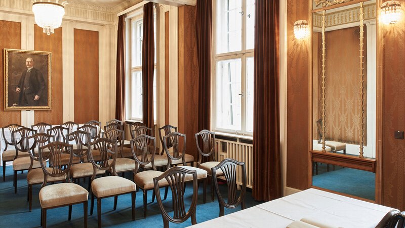 Eleganter Raum mit blauen Teppichboden, Stuhlreihen, einem Tisch mit wei&szlig;em Tuch und einem Gem&auml;lde an der Wand., &copy; W&uuml;rttembergische Staatstheater Stuttgart