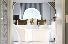 Elegantes Badezimmer mit freistehender Badewanne, dekorativen Kissen und einem runden Fenster im Hintergrund., © Waldhotel Stuttgart GmbH Elegantes Badezimmer mit freistehender Badewanne, dekorativen Kissen und einem runden Fenster im Hintergrund., © Waldhotel Stuttgart GmbH