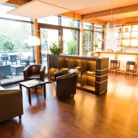 Moderne Hotel-Lounge mit Bar, Ledersesseln und gro&szlig;en Fenstern. Drau&szlig;en ist eine Terrasse mit Sitzgelegenheiten sichtbar., &copy; ARNOTEL GmbH